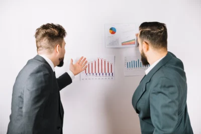 Dois homens de terno analisando gráficos em um ambiente de negócios, ilustrando a importância da confiança em decisões difíceis.
