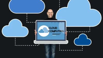 Profissional de tecnologia segurando um laptop exibindo 'Cloud Computing' com várias nuvens digitais ao fundo, simbolizando a influência da computação em nuvem na transformação digital das empresas.