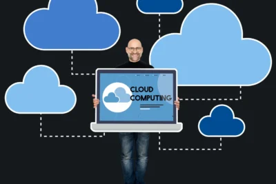 Profissional de tecnologia segurando um laptop exibindo 'Cloud Computing' com várias nuvens digitais ao fundo, simbolizando a influência da computação em nuvem na transformação digital das empresas.